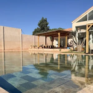 Piscine calme entourée de murs en terre cuite et d’oliviers dans une villa de retraite bien-être au Maroc
