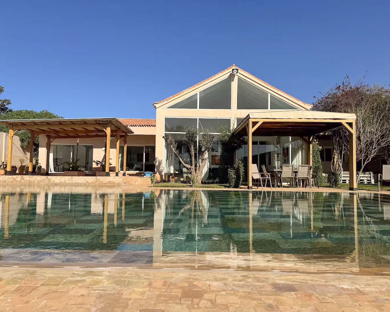 Maison principale de la retraite Ômri à Tamaris avec piscine, terrasse et grande baie vitrée sous un ciel bleu