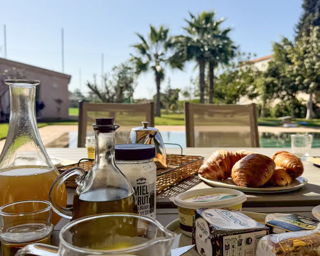 Petit-déjeuner en terrasse au bord de la piscine, avec viennoiseries, jus frais, miel et produits locaux à la retraite Ômri