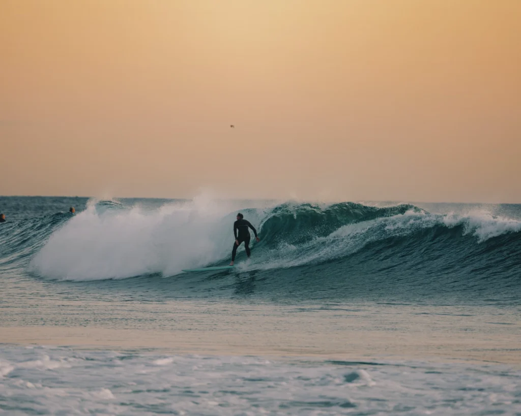 Surfeur au coucher du soleil sur la plage de Tamaris au Maroc, expérience bien-être Ômri
