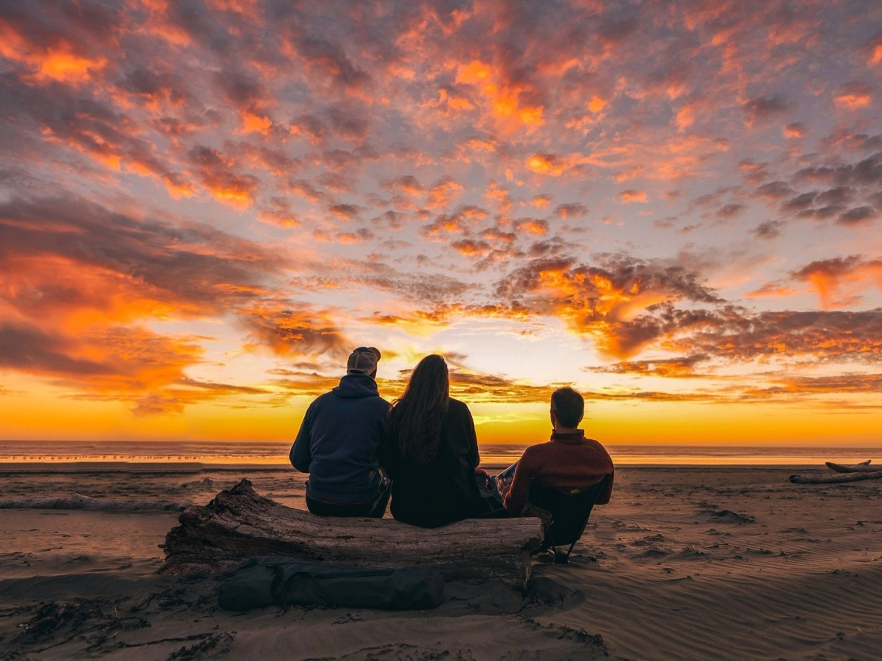 Trois personnes assises face à un coucher de soleil sur une plage paisible lors d'une retraite bien-être au Maroc